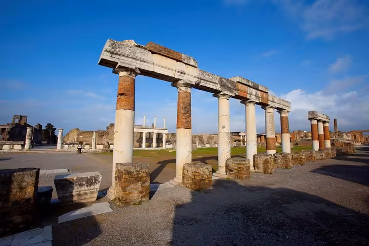 Explore ancient columns at Pompeii ruins under a clear blue sky, a must-see on your Positano to Pompeii tour.