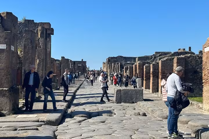 Visitors exploring ancient streets of Pompeii under a clear blue sky, capturing the essence of historic Italy tours.