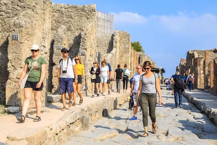 Tourists exploring ancient streets of Pompeii under a clear blue sky on a Full-Day Pompeii and Vesuvius Tour.