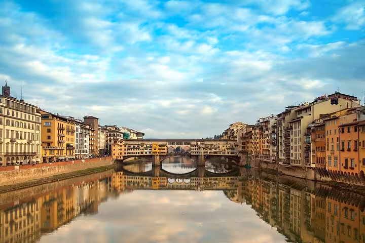 Scenic view of Ponte Vecchio reflecting in the Arno River, surrounded by historic Florence architecture.