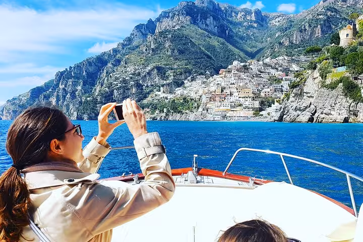 Traveler capturing stunning views of Positano's colorful cliffside from a classic Gozzo boat tour.