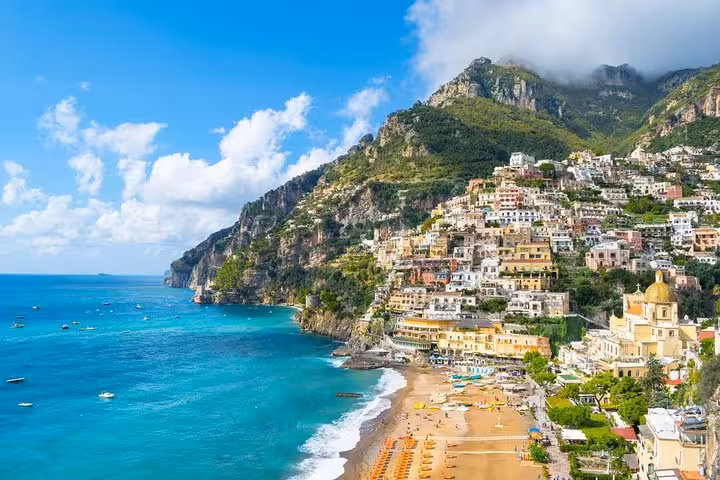 Stunning view of Positano's colorful cliffside buildings and sandy beach on the Amalfi Coast under a bright blue sky.