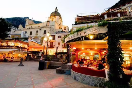 Evening piazza dining in Positano with glowing trattorias and dome church on From Dusk Till Night experience