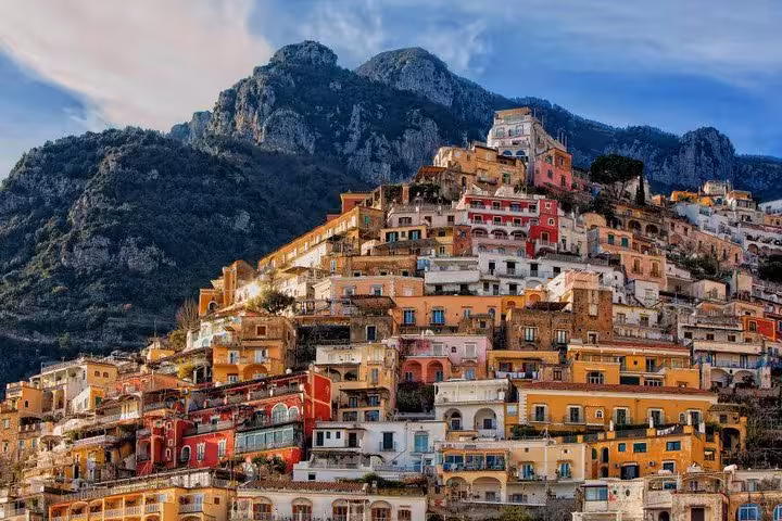 Picturesque Positano hillside with charming pastel buildings against dramatic mountain backdrop.
