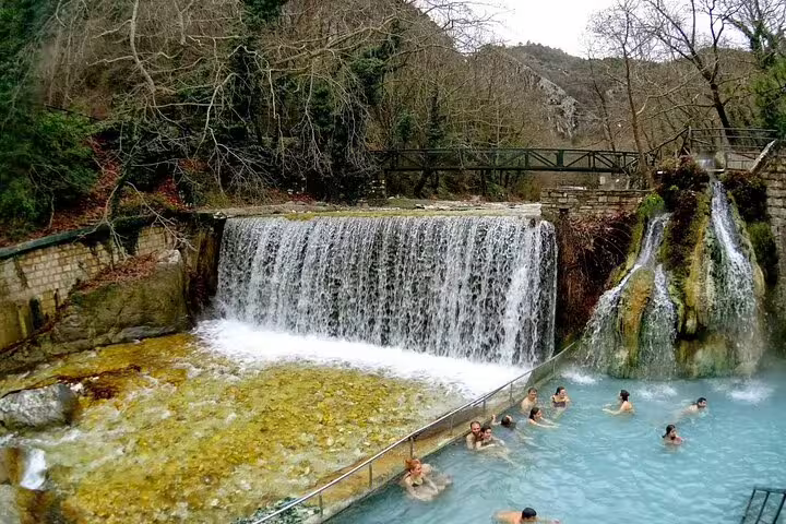 Travelers relaxing in Pozar Hot Baths thermal pools beneath a waterfall on a private ride from Thessaloniki