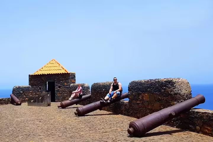 Tourists enjoy sunny day sitting on historic cannons at Praia fort, ideal for scenic views and cultural exploration.