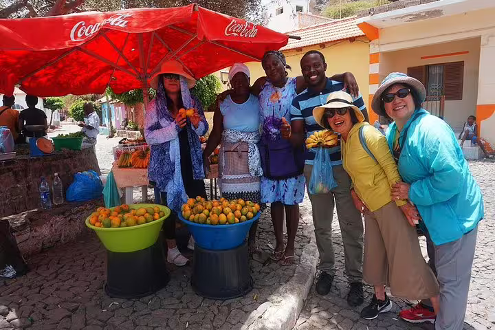 Tourists enjoying local market with fresh fruits under vibrant umbrellas during Praia by Night tour.