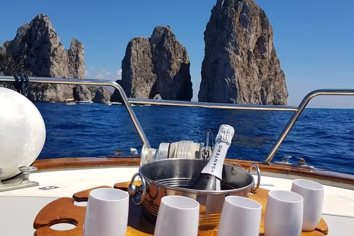 Champagne and glasses on a boat with a stunning view of Capri's iconic Faraglioni rocks on a private tour.
