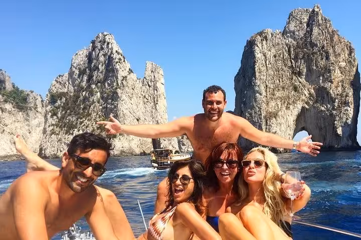 Group enjoying a sunny day on a private boat tour near the iconic Faraglioni rocks in Capri.