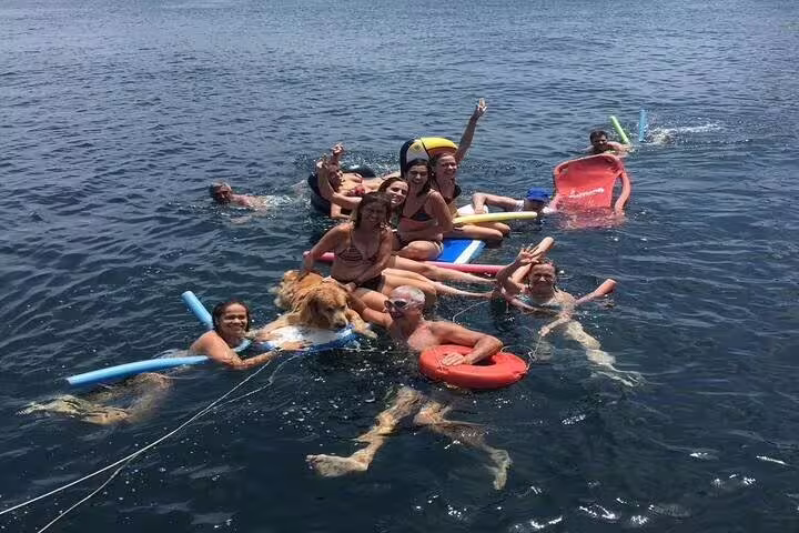 Group enjoying a private boat tour in Rio, floating with inflatables and a dog in the ocean, perfect for summer fun.