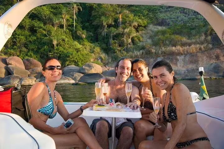 Happy group enjoying champagne and barbecue on a private boat tour in Rio, surrounded by lush greenery and rocky shores.