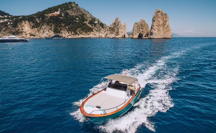 Private boat speeding across the blue sea between Sorrento and Positano with Capri cliffs and Faraglioni rocks in view