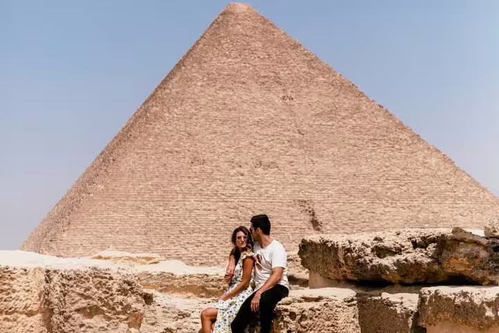 Travelers sitting near the Great Pyramid of Khufu on a private guided Giza tour with transfers and tickets included