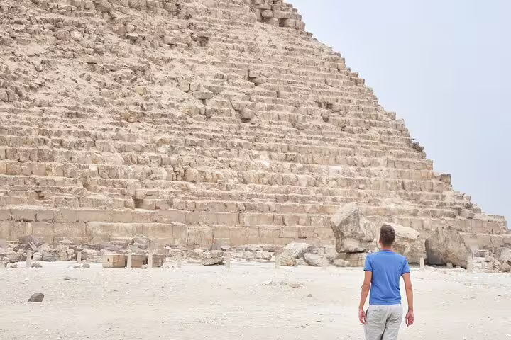 Traveler at the base of the Great Pyramid of Giza on a private guided tour with transfers and tickets included