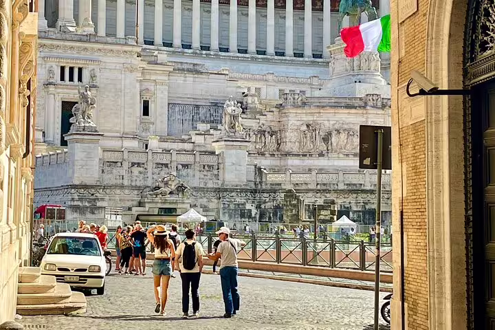 Travelers on a private guided walking tour approach the Vittoriano monument in central Rome with Italian flag waving nearby