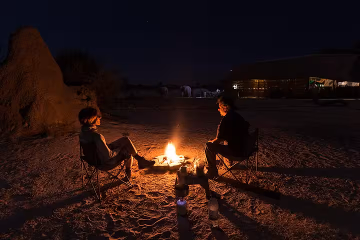 Two people enjoy a campfire under the starry sky during a private Liwa overnight desert safari experience.
