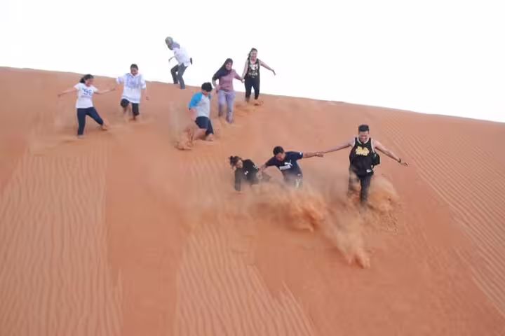 Group enjoying thrilling sand dune descent during a private tour in Oman, offering an exciting desert adventure.