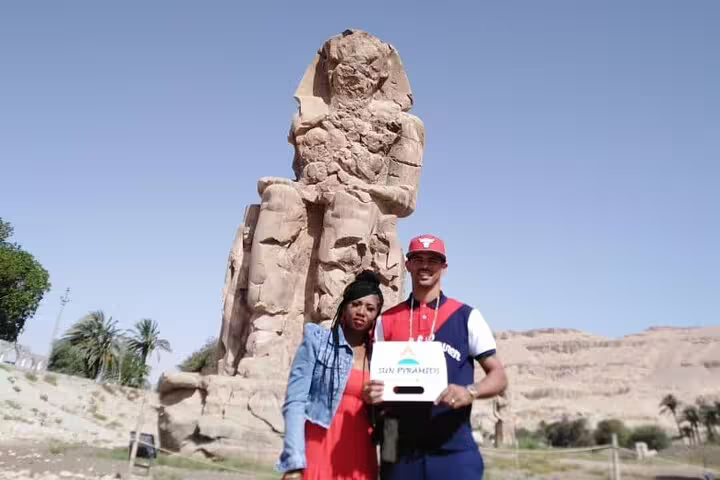 Travelers pose by the Colossi of Memnon on a private overnight Luxor tour from Cairo by flight