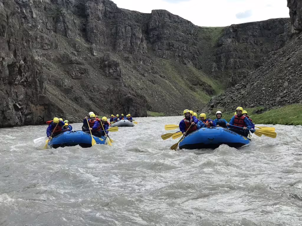 Adventurous private rafting group navigating the thrilling rapids of West Glacial River with scenic canyon views near Akureyri.