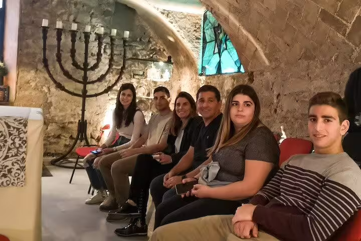 Visitors seated in a historic room with a large menorah, part of a private religious tour exploring Sagrada Familia, Romans, and Jewish Quarter.