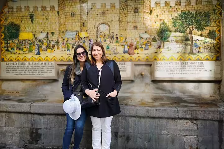 Two women smiling in front of a historic mural in the Jewish Quarter, part of the Private Religious Tour featuring Sagrada Familia.