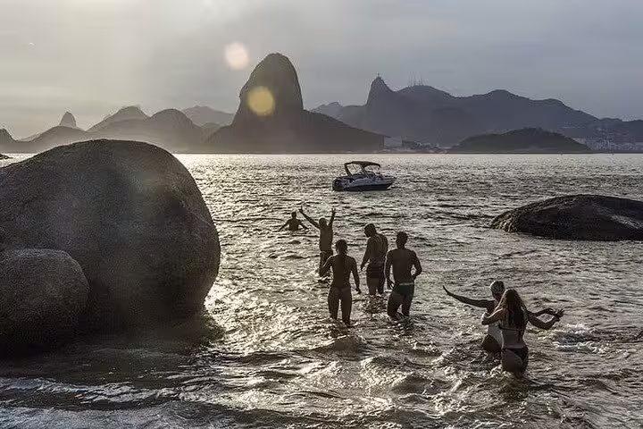 Group enjoying a sunset swim near Sugarloaf Mountain on a private Rio boat tour with barbecue and drinks.
