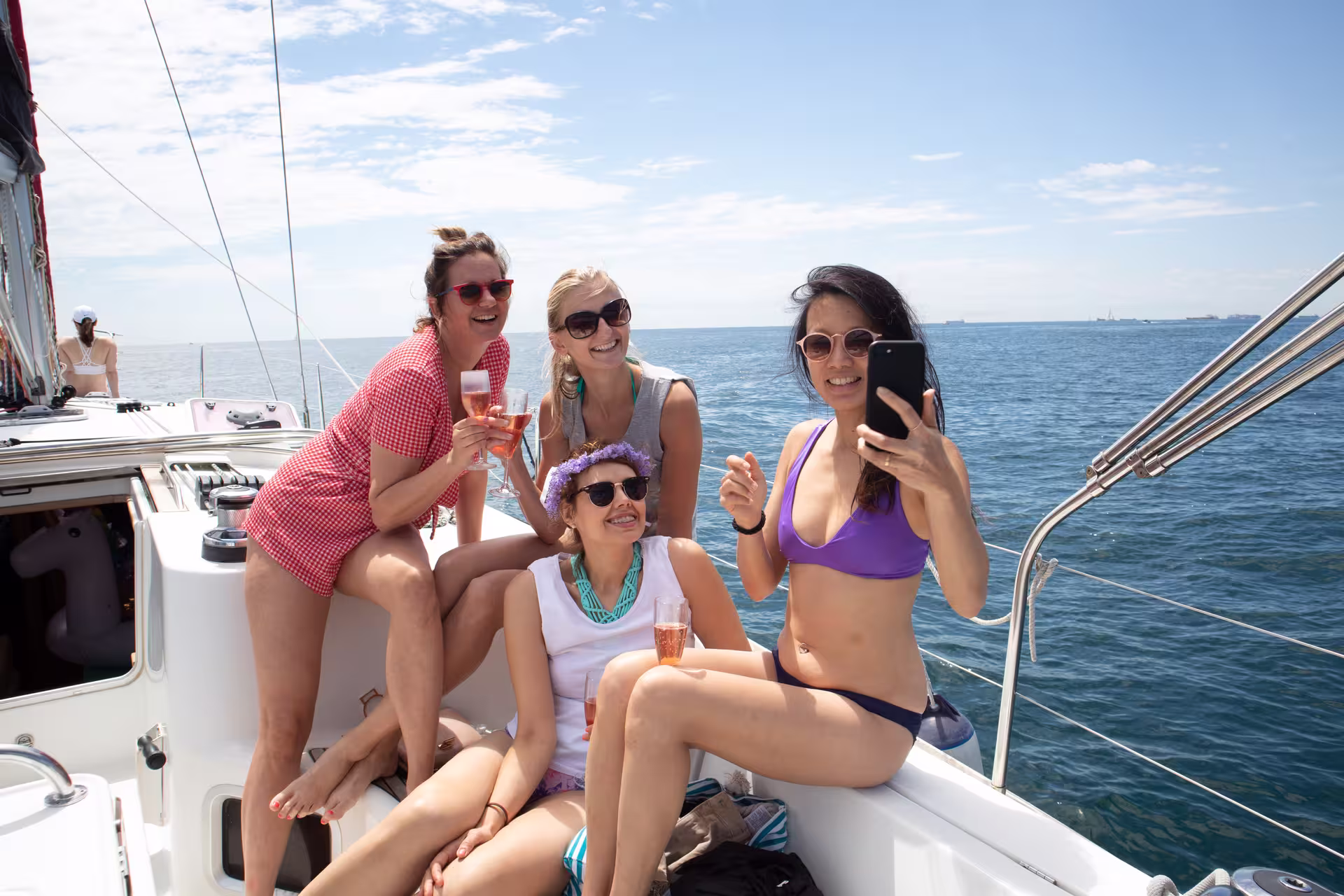 Group of friends enjoying a sunny day on a private sailing boat in Barcelona, capturing memories with drinks and smiles.