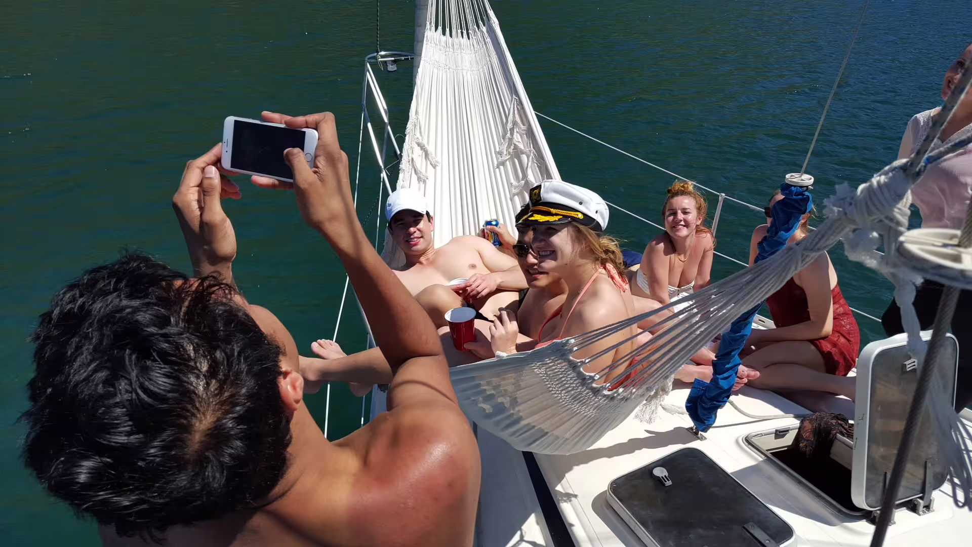 Group of friends enjoying a private sailing tour on MAKANI MAIKAI with drinks and a hammock on sunny waters.
