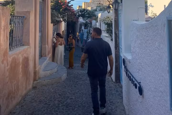 Private Santorini tour guide leading guests through a cobblestone alley in a traditional village at sunset