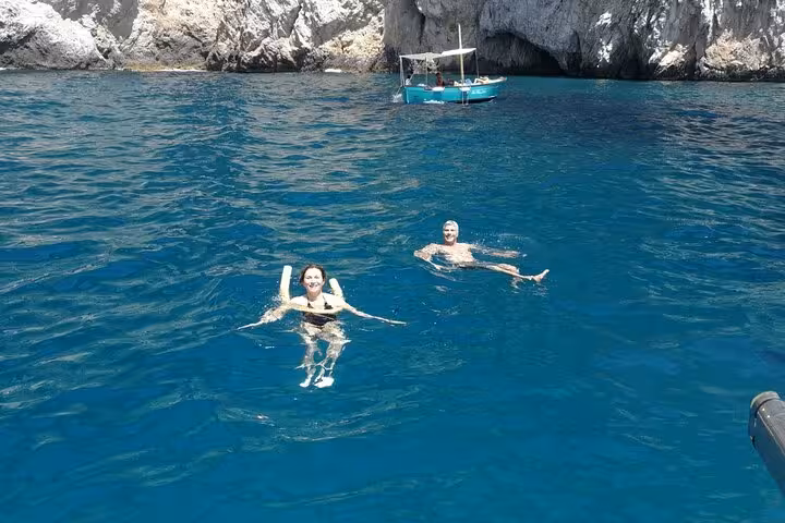 Two people swimming in clear blue waters near a boat during a private sunset boat tour at a scenic coastline.