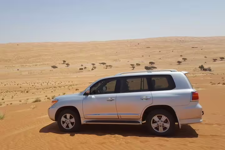 Silver SUV parked on the golden dunes of Wahiba Sands Desert, showcasing private transfer from Muscat adventure.