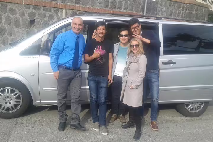 Happy small group posing with their driver beside a modern minivan during a private Sorrento to Naples transfer service
