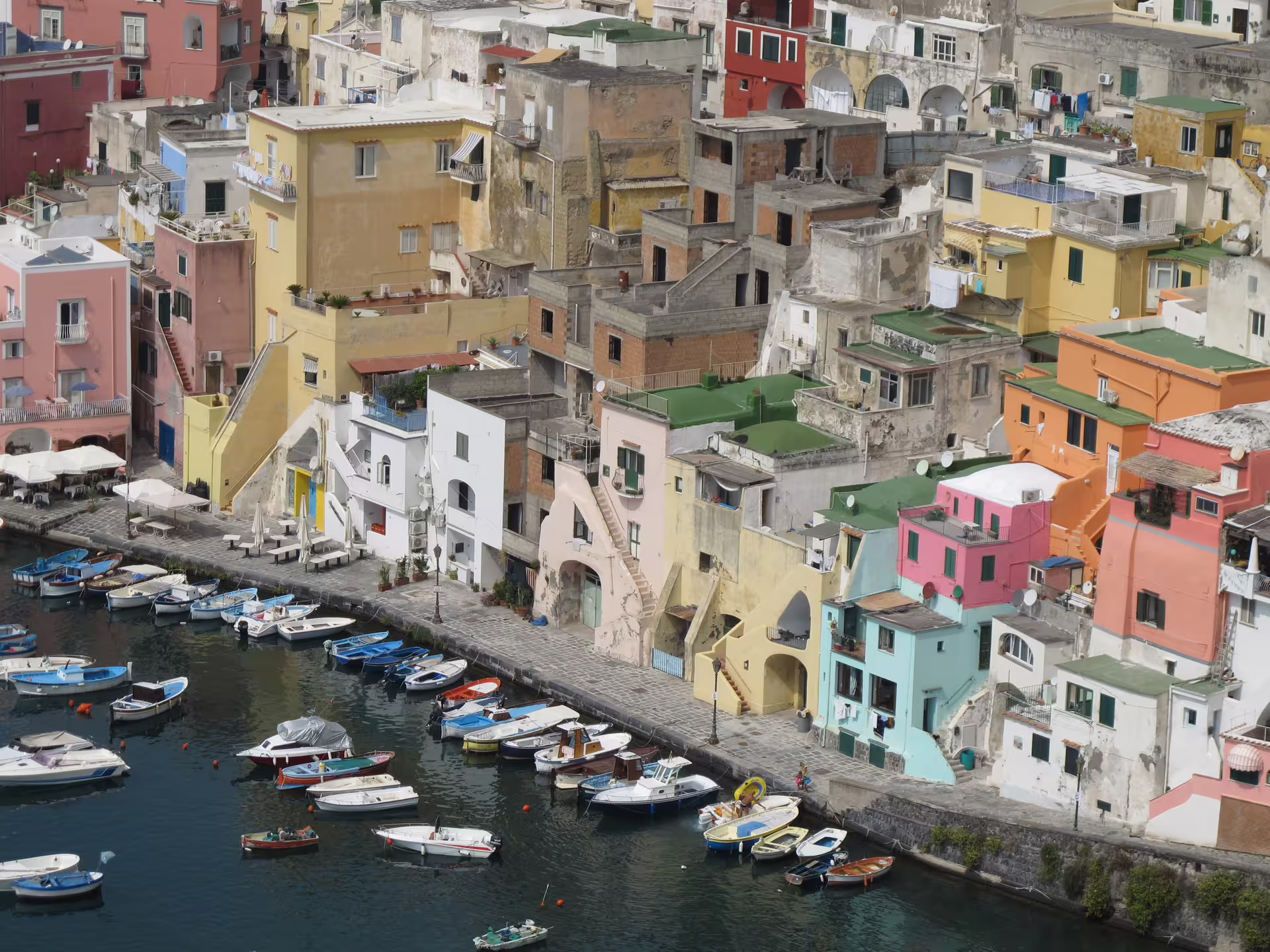 Colorful cliffside houses and moored boats in Marina di Corricella on Procida, seen from a luxury full day catamaran tour