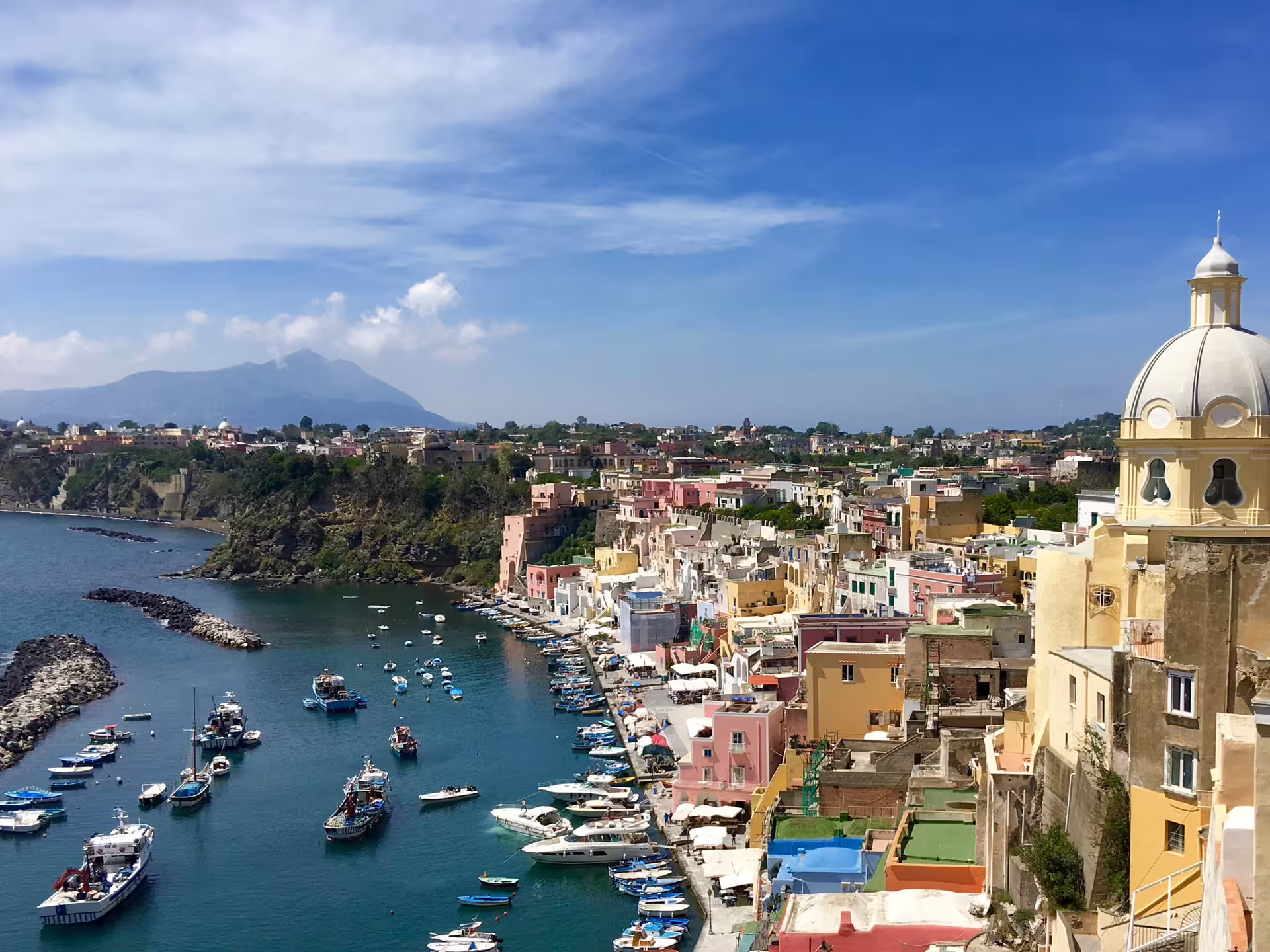Panoramic view of Procida’s pastel marina, domed church and boats from the sea on an exclusive full day catamaran cruise