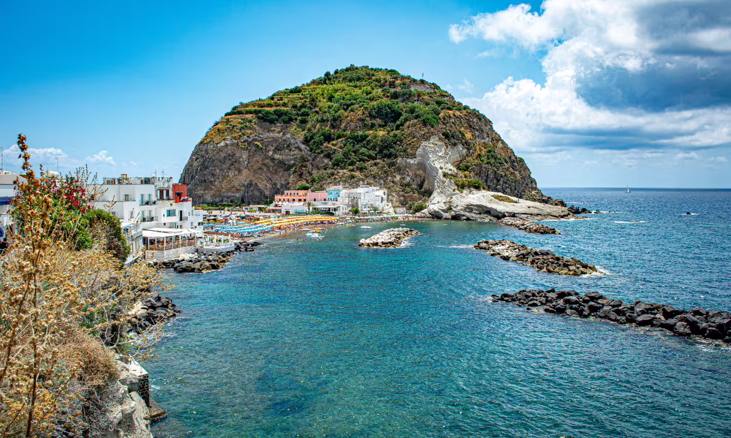 Rocky cove and beach clubs near Procida with dramatic cliffside village and clear Tyrrhenian Sea views on a luxury boat tour