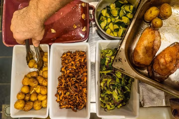 Hands plating roasted potatoes, zucchini and duck for a Provençal cooking class with exceptional chef in Avignon
