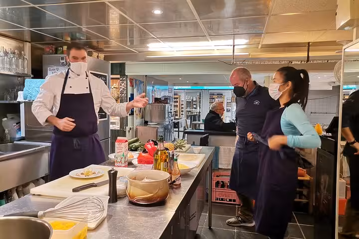 Guests in aprons and masks learning Provençal recipes in Avignon cooking workshop kitchen with chef