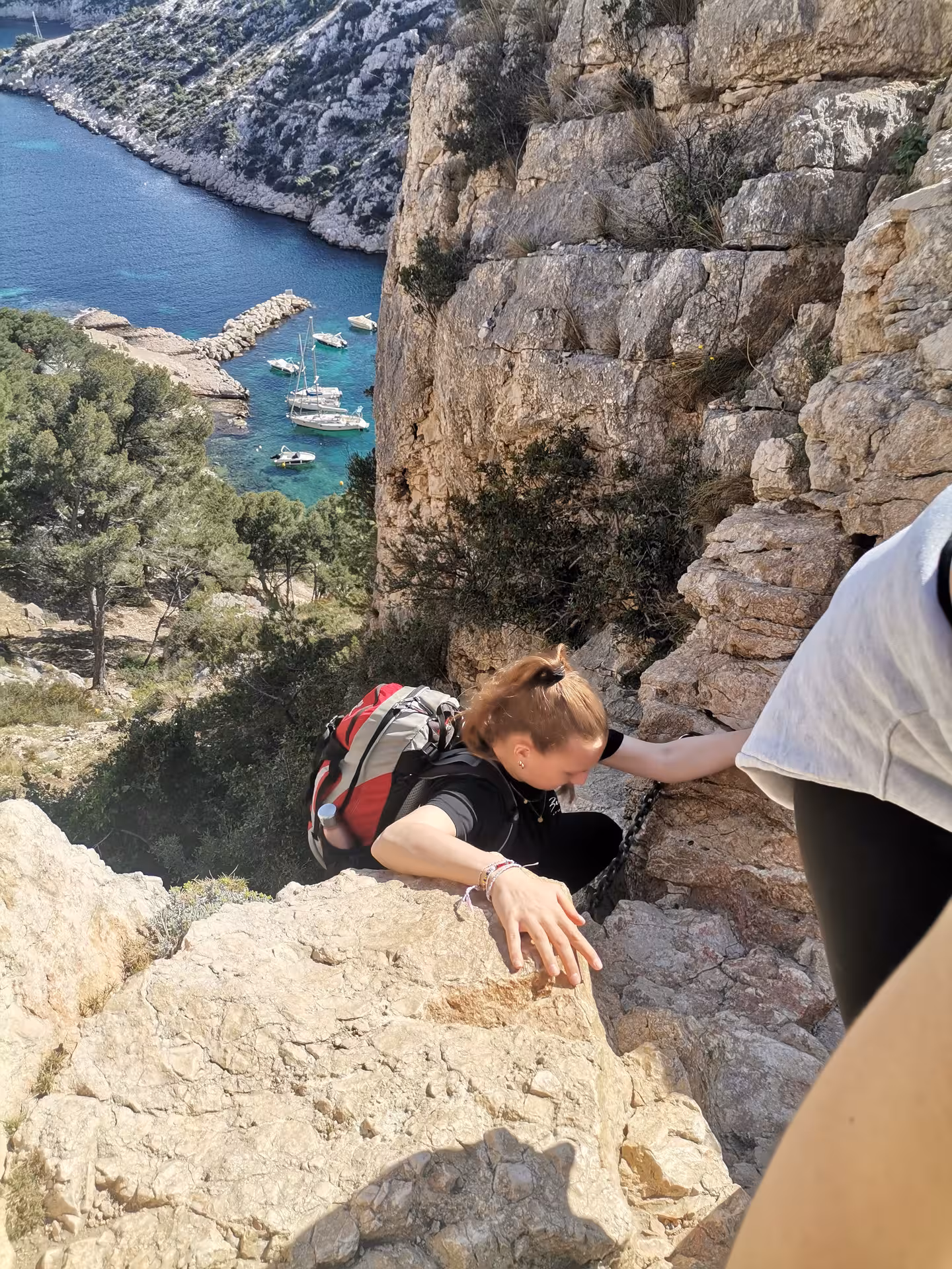 Scrambling above a turquoise Calanques cove in Provence, hikers on coastal cliffs during a 7-day trek