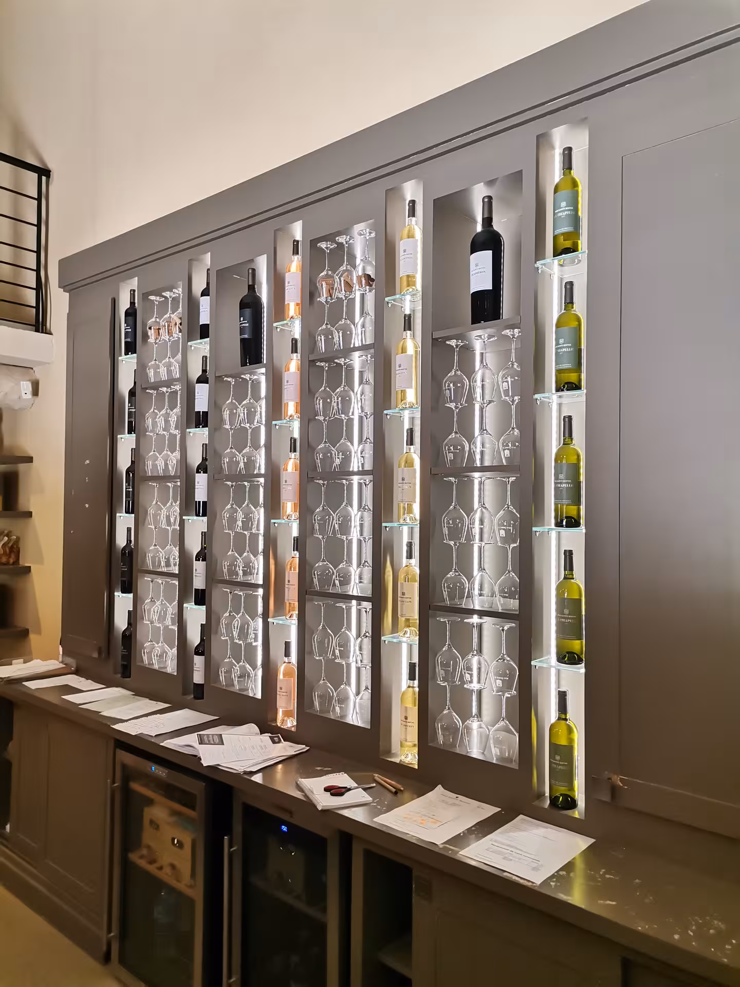 Backlit wall of wine bottles and glasses in a Provence winery, part of Arles and Les Baux-de-Provence tour