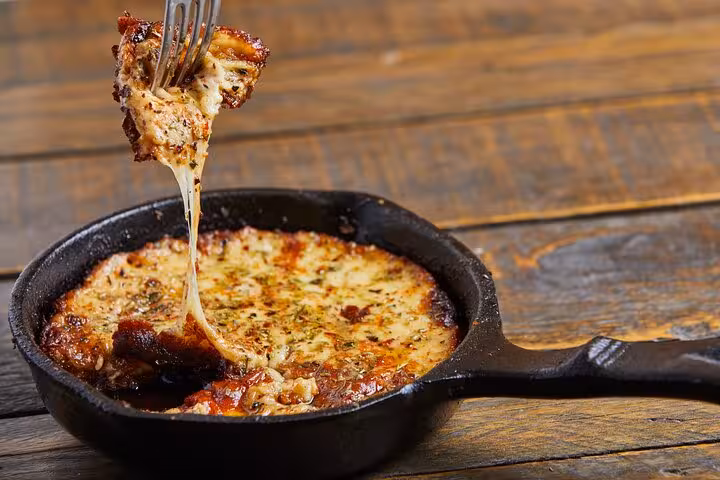 A fork lifting a cheesy slice of provoleta from a sizzling skillet, showcasing traditional Argentinian comfort food.