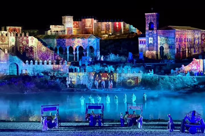 Nighttime Puy du Fou spectacle with illuminated castle projections and performers, private minivan transfer option