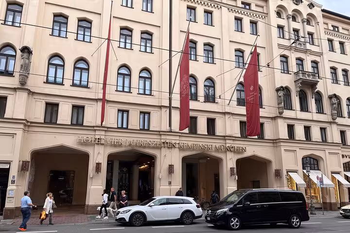 Elegant Munich hotel facade with red flags, bustling street view, perfect for cruise terminal transfers.