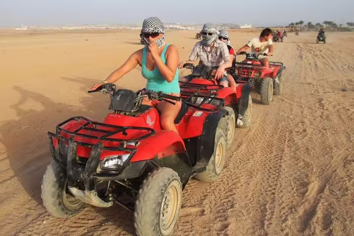 Group riding red ATV quad bikes across Hurghada sand dunes, guided desert safari adventure tour from hotel