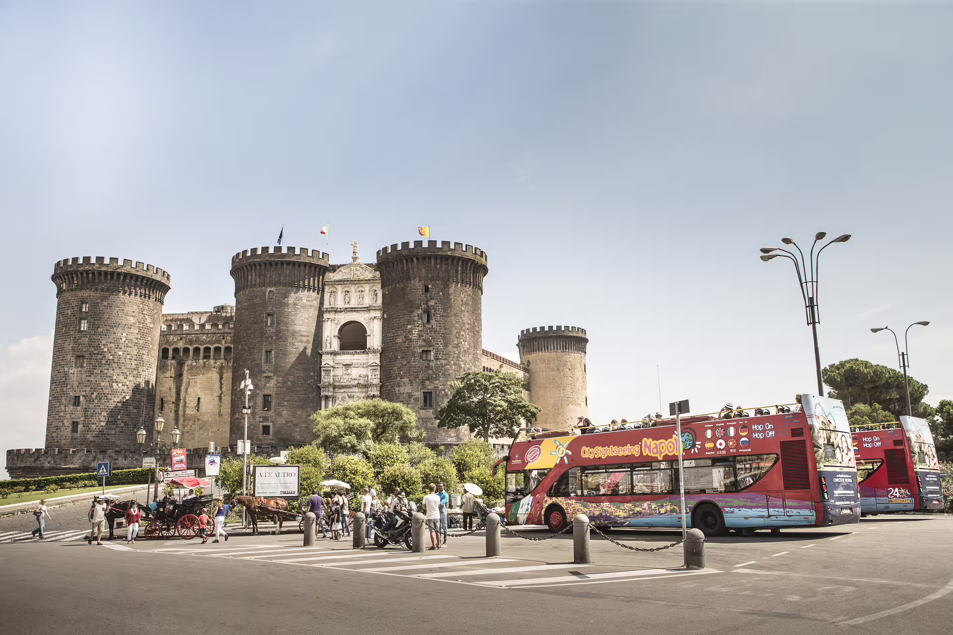 Red hop on hop off sightseeing bus at Castel Nuovo Maschio Angioino, a top Naples city tour stop in historic center