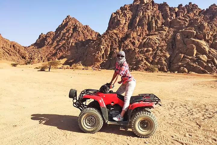 Rider on red quad bike safari in Sinai desert mountains, Sharm El Sheikh ATV tour with scenic rocky backdrop
