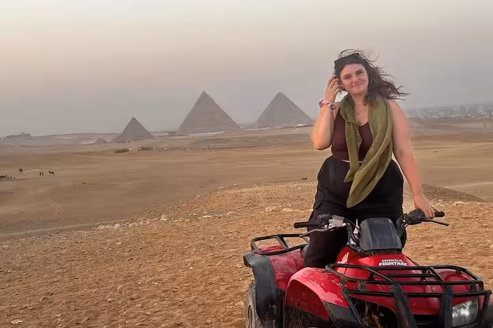 Rider on red quad bike in Giza Desert with Great Pyramids backdrop, ATV tour with transfers and drinks