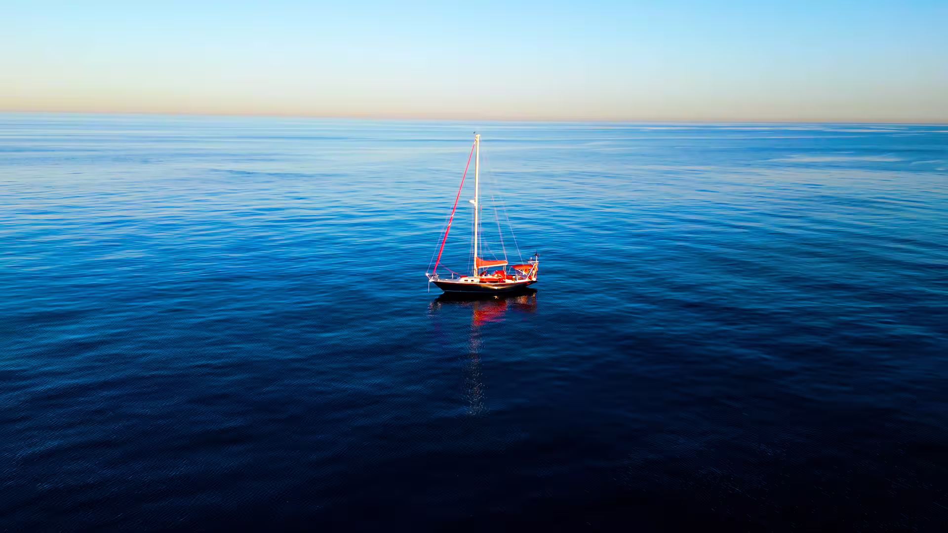 El velero rojo Assol flotando en medio del mar Mediterráneo, con un horizonte lejano y un cielo despejado que se funde con el agua, creando