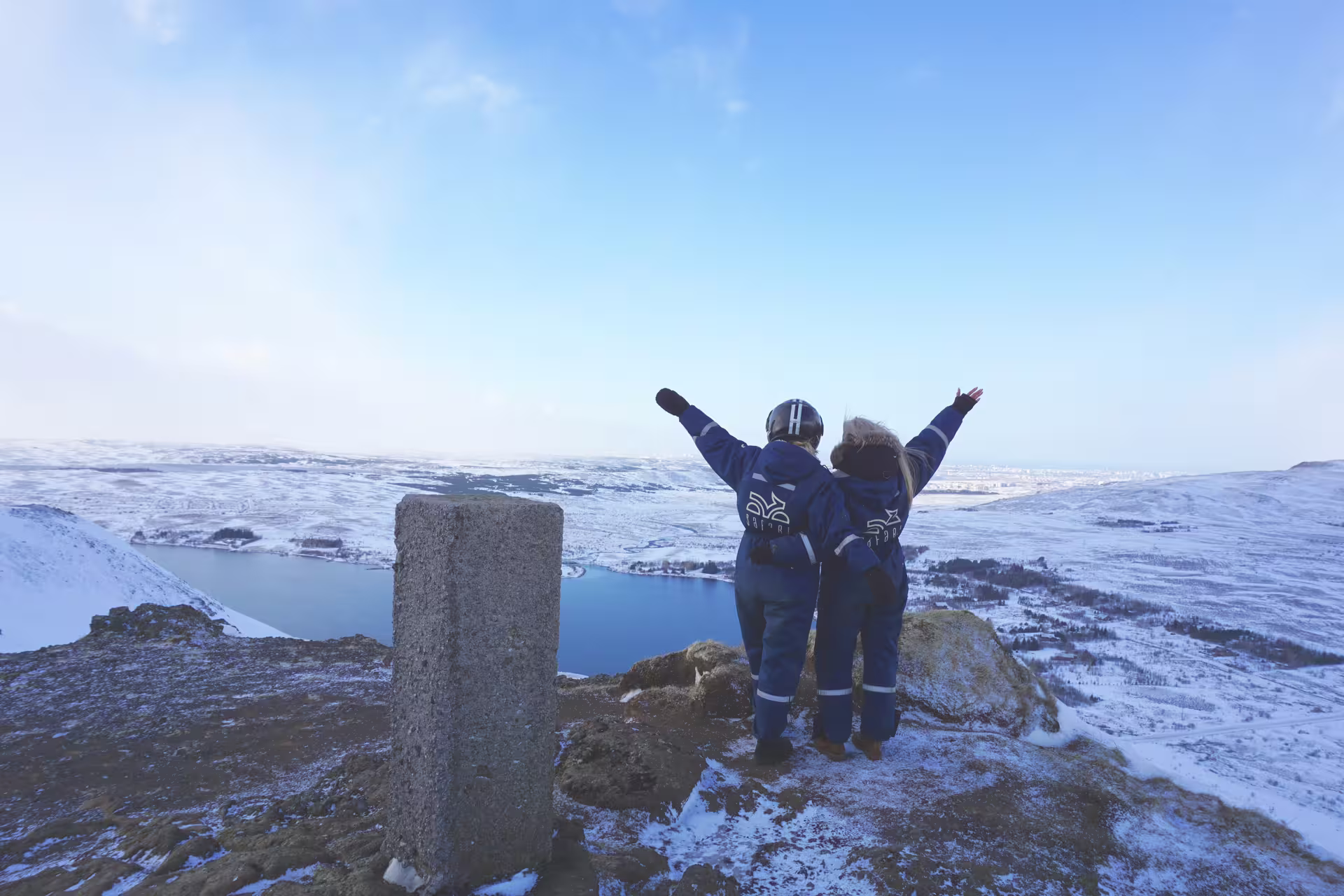 Two people in winter gear celebrate a breathtaking snowy view over Reykjavik on an exhilarating ATV adventure.