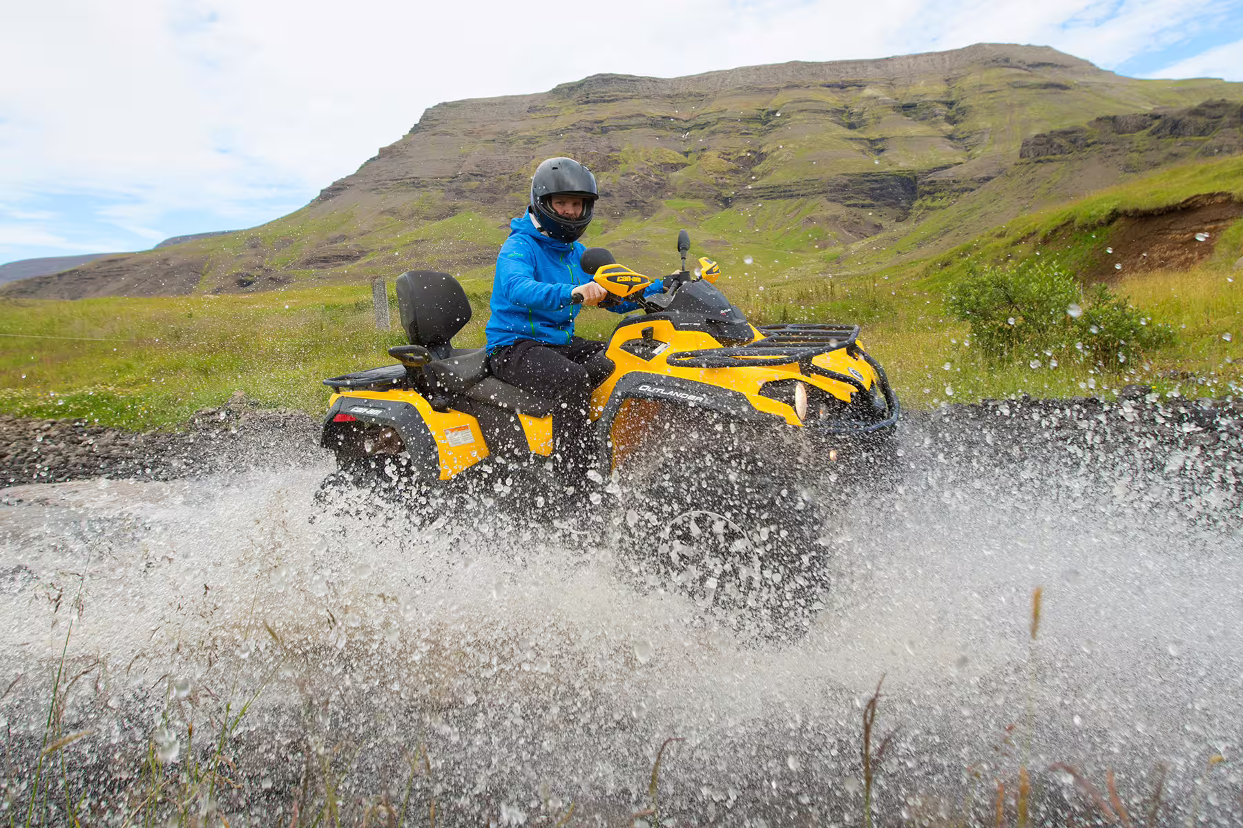 ATV rider splashes through water on a scenic trail near Reykjavik, showcasing thrilling adventure in Iceland's rugged landscape.