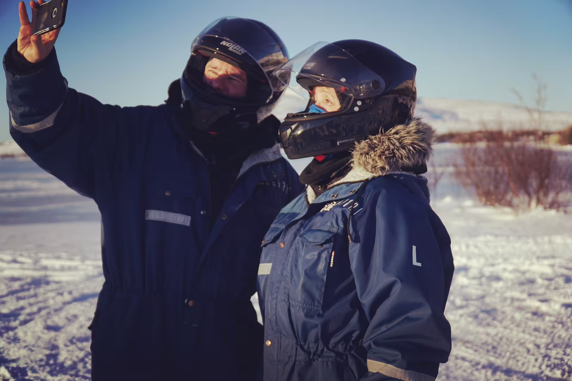 Two people in helmets and winter gear take a selfie in snowy Reykjavik during a thrilling 1-hour ATV tour adventure.